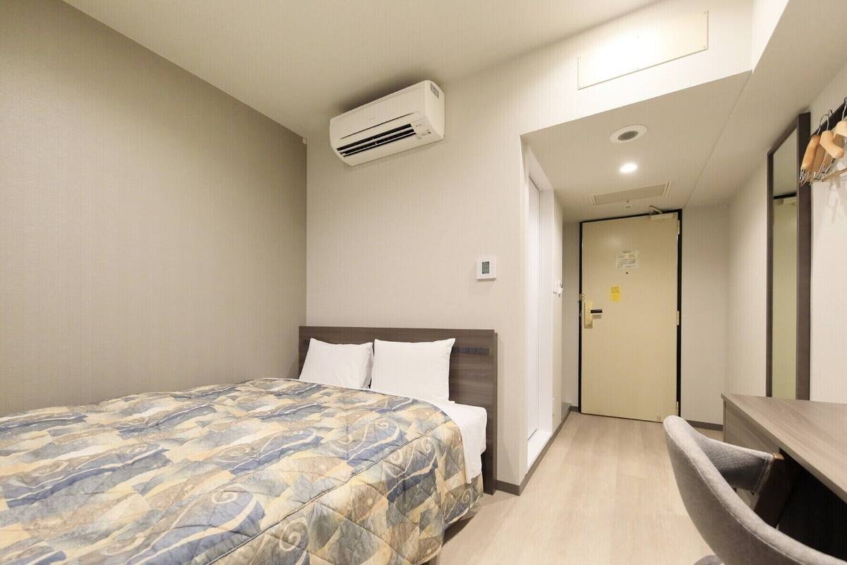 Una habitación de hotel con cama, escritorio, aire acondicionado y puerta.