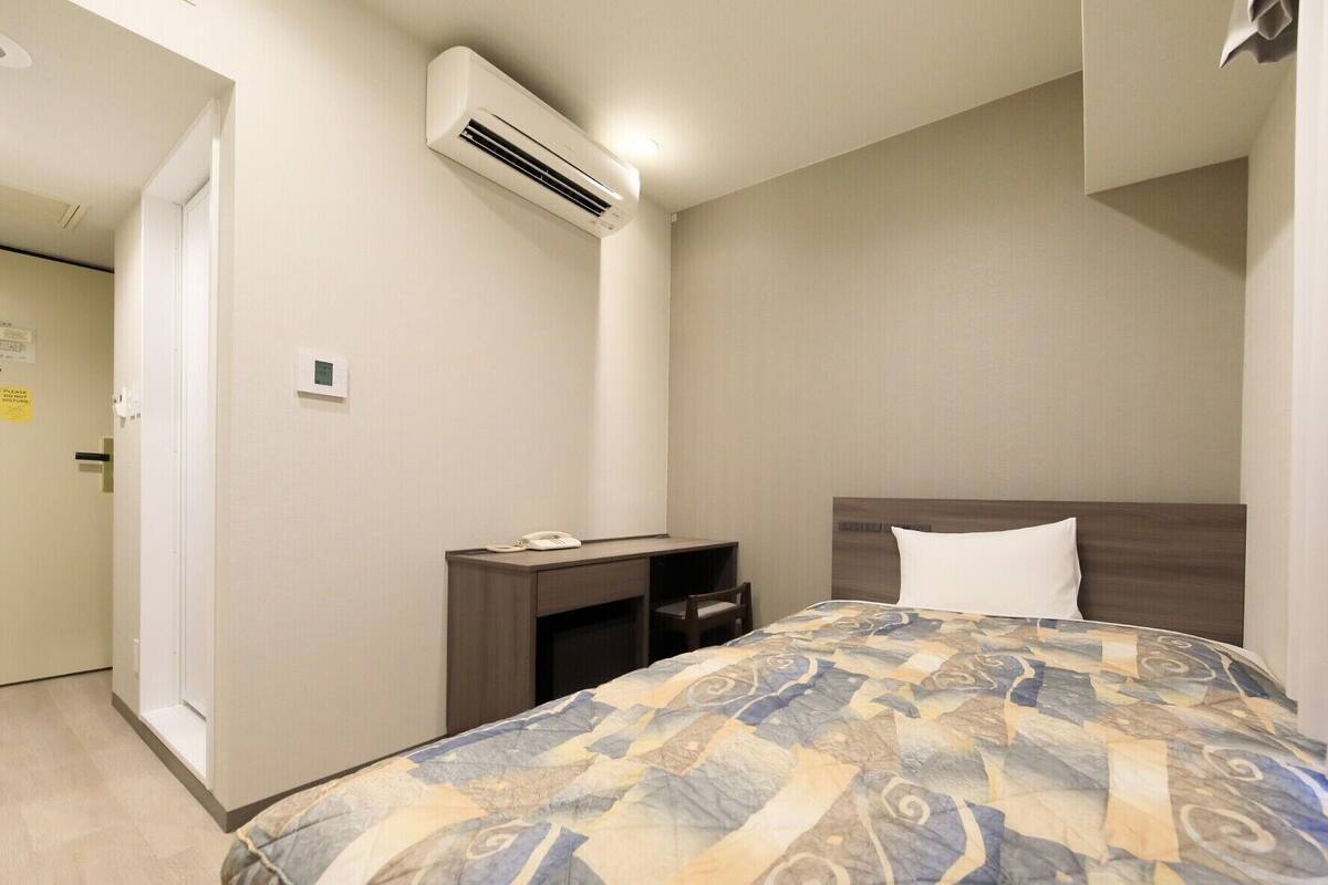 Habitación de hotel con cama, escritorio, silla, unidad de aire acondicionado y teléfono en el escritorio.