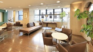 Un espace lounge moderne avec des canapés en cuir, des tables et des fauteuils ronds, de grandes fenêtres offrant une vue sur la ville et un plancher en bois.