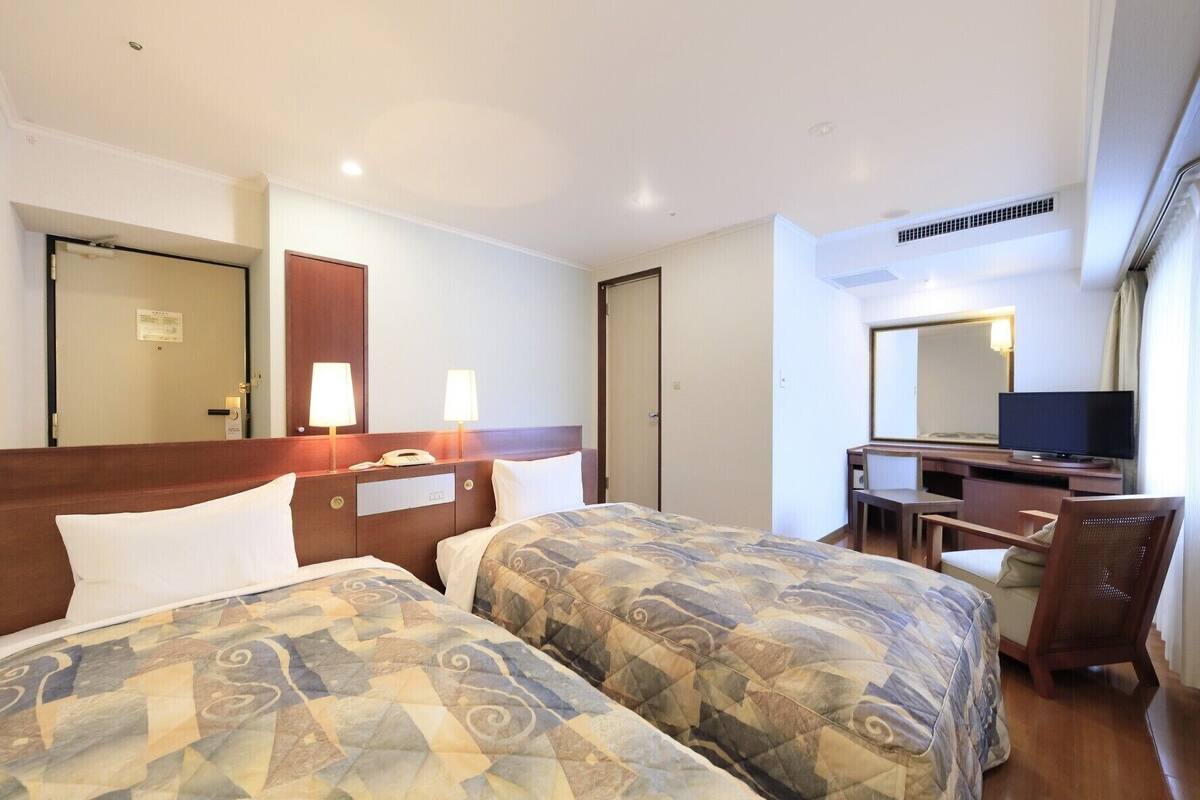 Una habitación de hotel con dos camas, un escritorio, una silla, un televisor y un espejo.