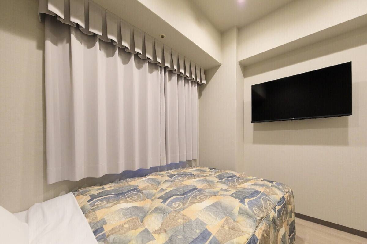Un dormitorio con cama, cortinas, un televisor de pantalla plana y una colcha estampada.