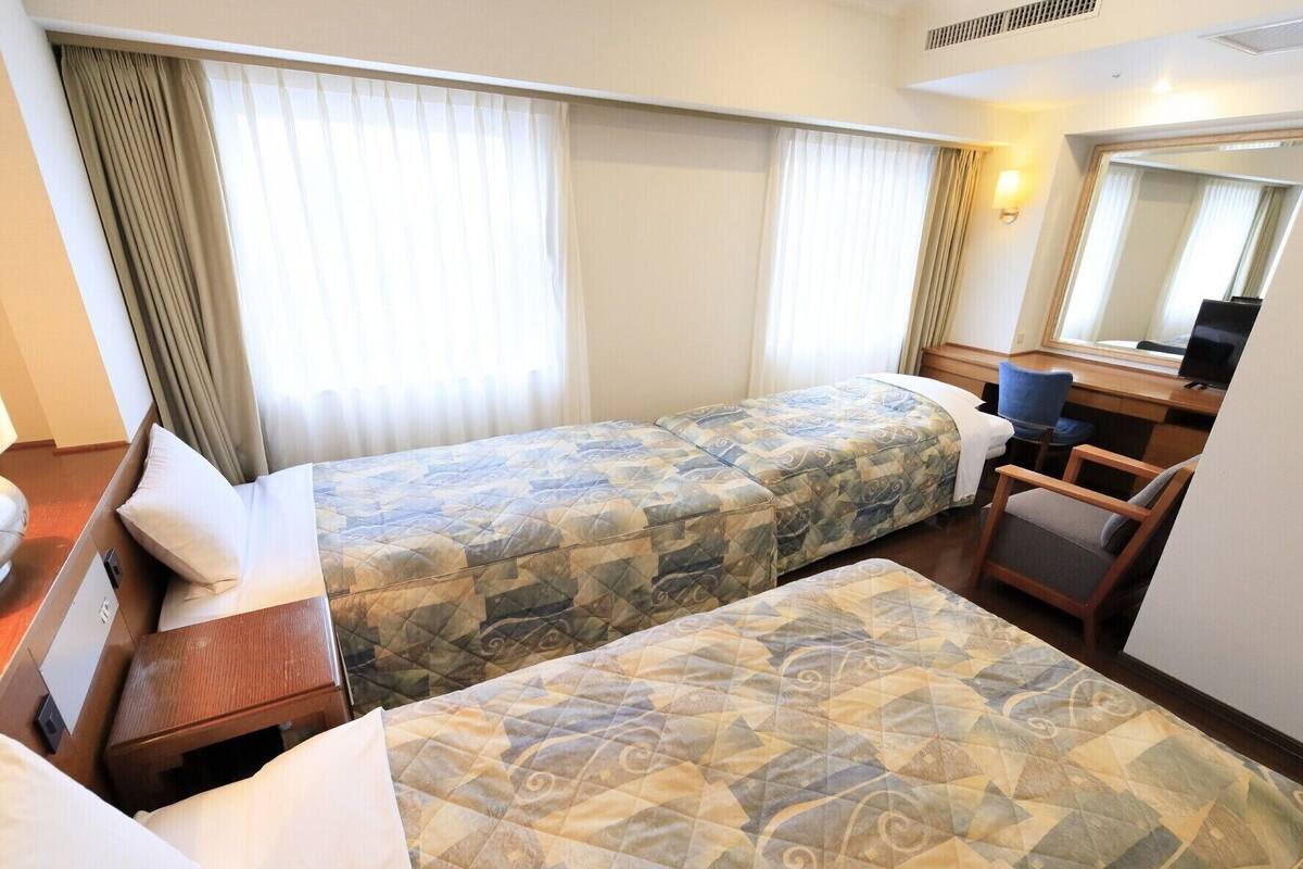 Habitación de hotel con dos camas, un escritorio, una silla y un espejo grande.