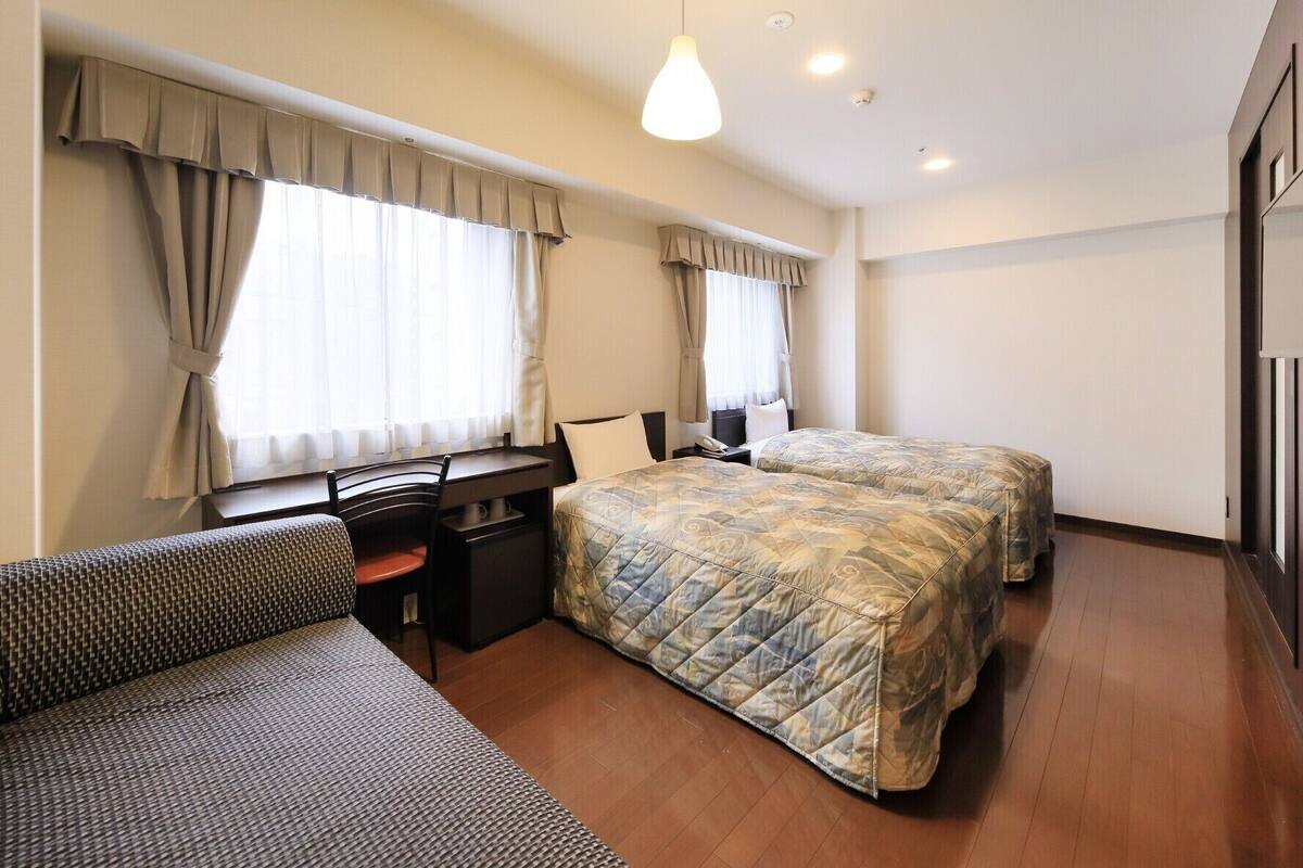 Habitación de hotel con dos camas, un escritorio, una silla y un sofá.