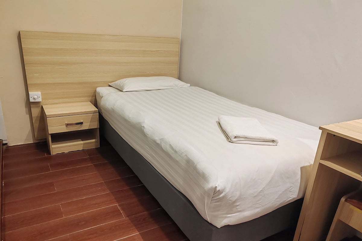 A single bed with a wooden headboard, a bedside table, and a nightstand.