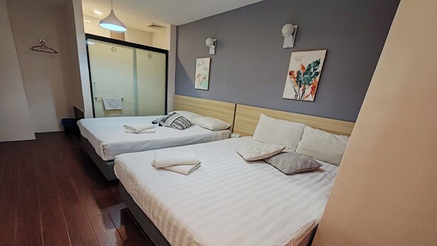 Habitación de hotel con dos camas, cabeceros de madera, una toalla sobre cada cama, y una pared con una planta y un aplique.
