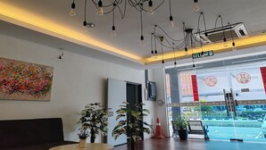 Un vestíbulo de hotel con diseño moderno, que presenta un mostrador de recepción, plantas en macetas y un cuadro abstracto y colorido en la pared.