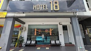 La entrada del Hotel 18 con una puerta de cristal, un coche aparcado fuera y un cartel sobre la entrada.