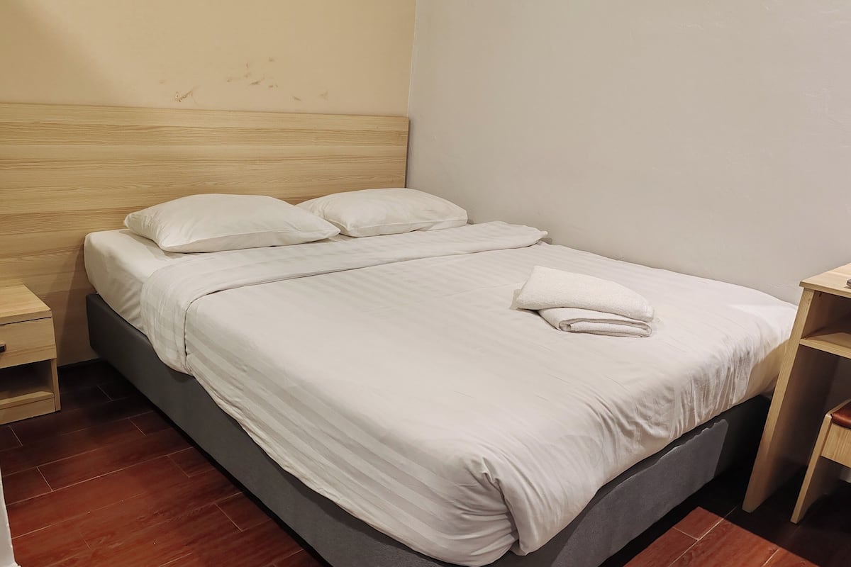 A neatly made bed with white linens and pillows, a wooden headboard, and a small bedside table with a drawer.