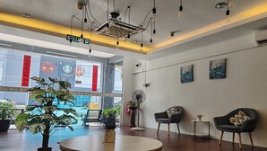 Un moderno vestíbulo de hotel con una mesa redonda de madera, sillas negras y blancas, plantas en macetas y obras de arte en las paredes.