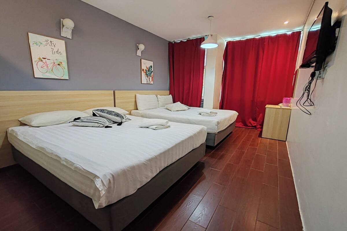 A hotel room with two beds, a wooden headboard, a small desk, and a TV mounted on the wall.