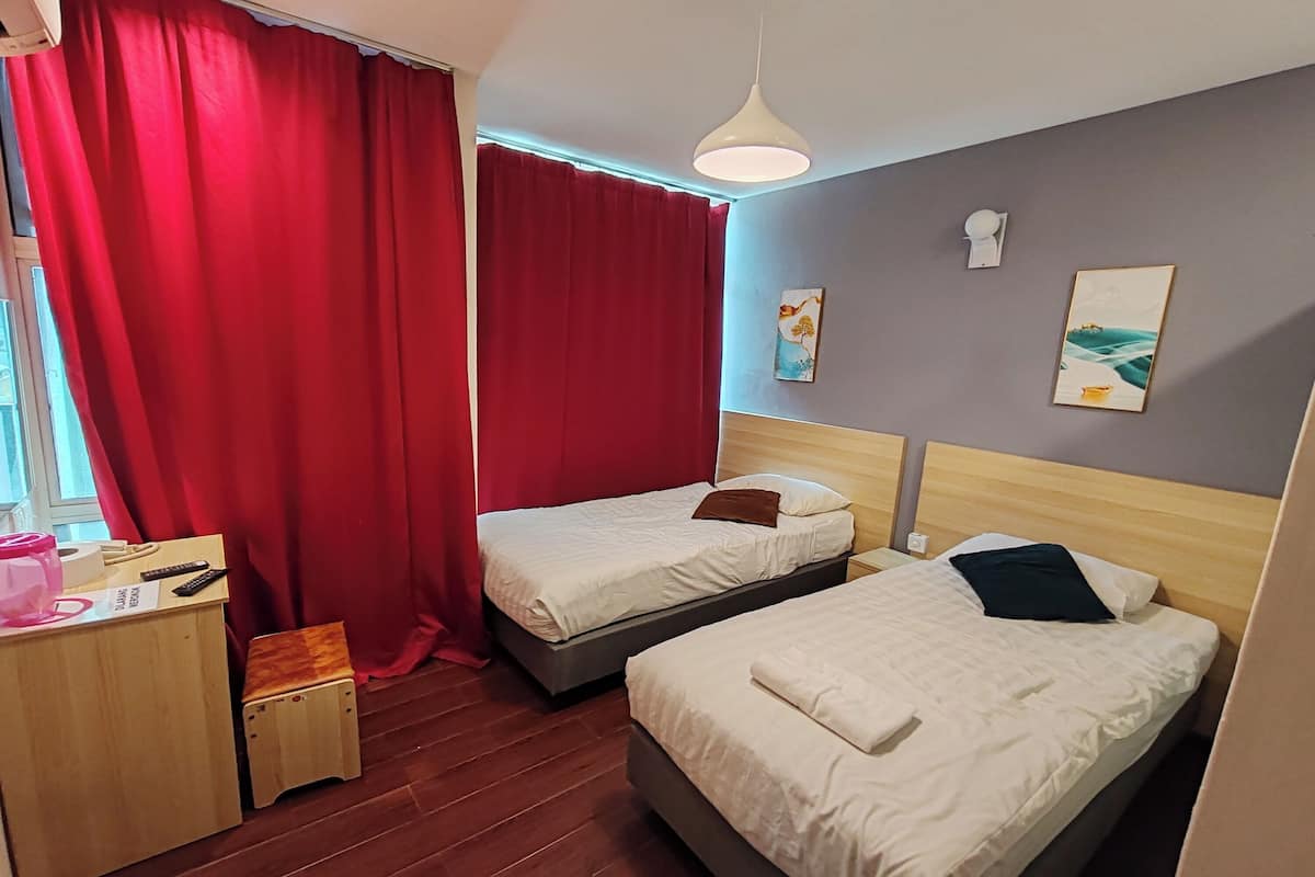 A hotel room with two beds, a wooden desk, a red curtain, and artwork on the wall.