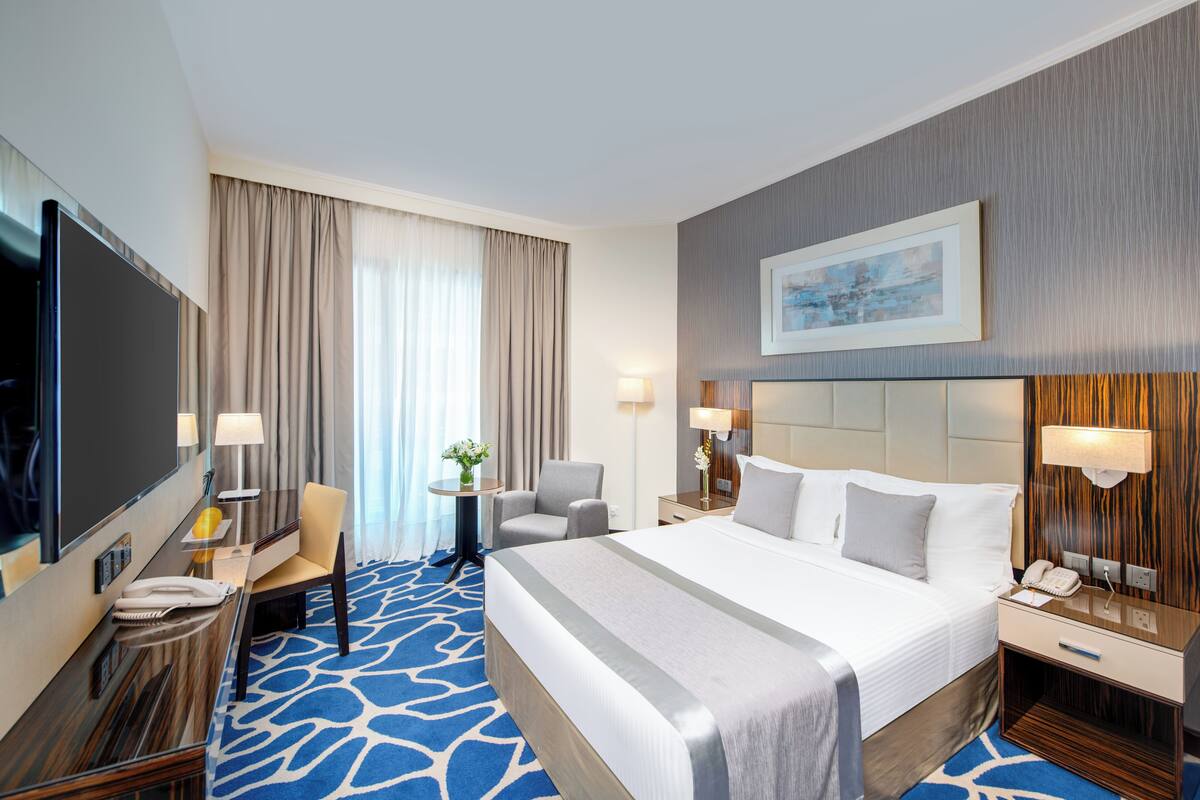 Une chambre d’hôtel avec un grand lit, un bureau avec une chaise, une télévision et une fenêtre avec des rideaux.