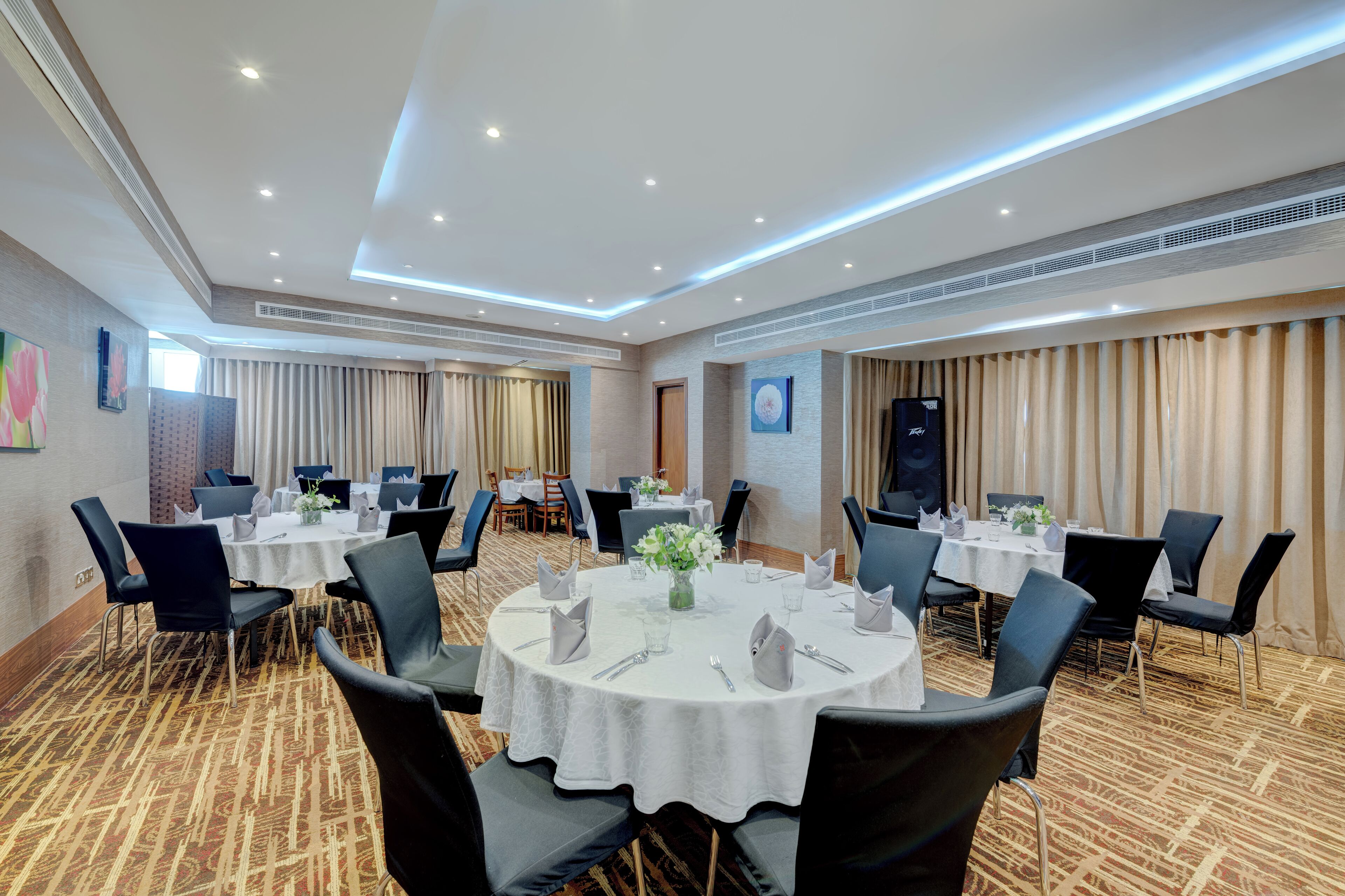 Une salle de conférence avec des tables rondes, des chaises noires et des nappes blanches.