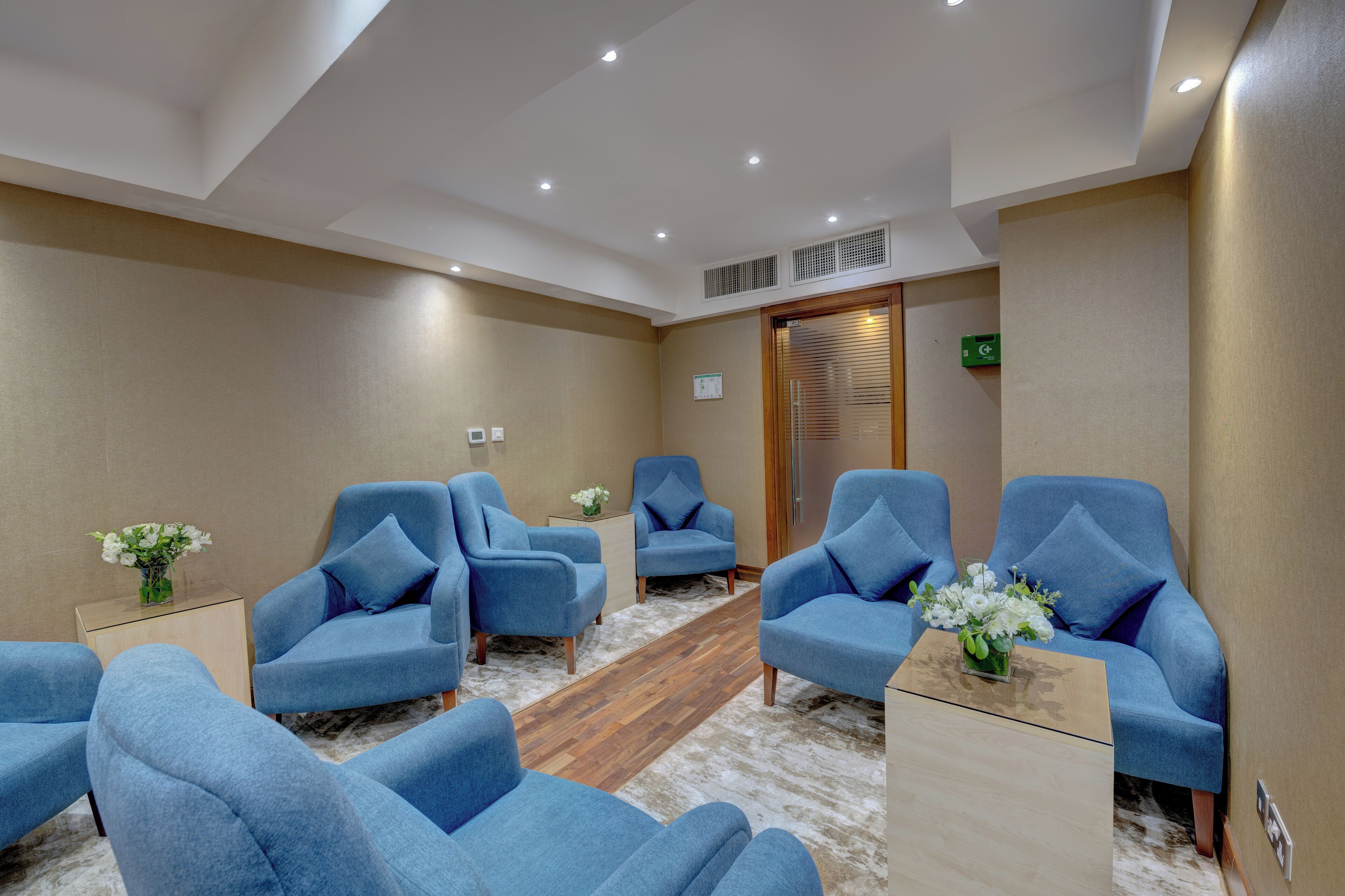 A room with six blue armchairs arranged in a semi-circle, a wooden floor, and a beige carpet.