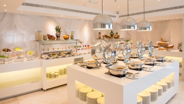 A buffet setup with multiple serving stations, glass shelves with food items, and hanging pendant lights. - Hawthorn Suites by Wyndham Abu Dhabi City Centre (Abu Dhabi)