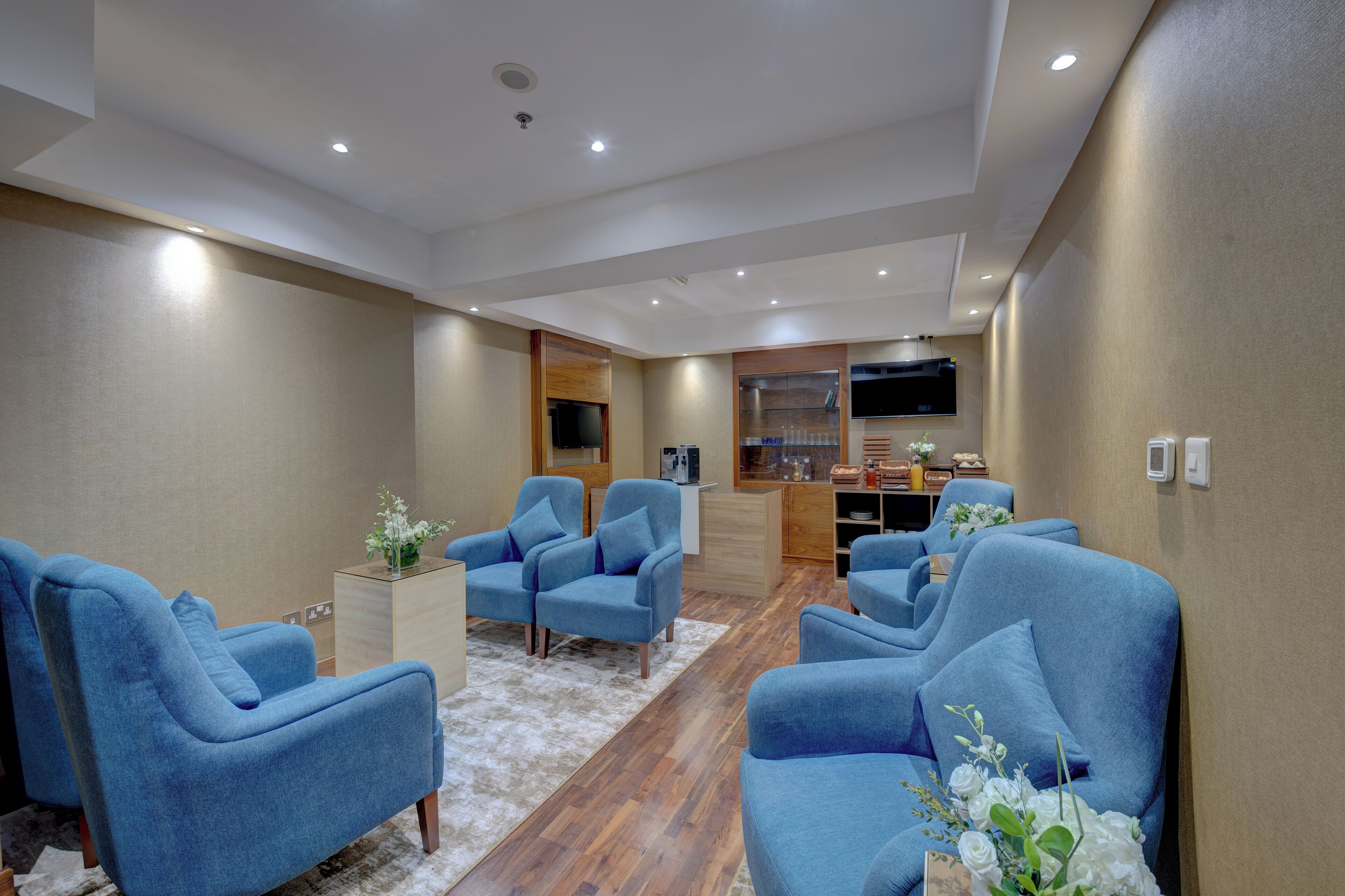 Ein modernes Wohnzimmer mit blauen Sesseln, einem Holzkabinett und einem flachbildfernseher an der Wand.