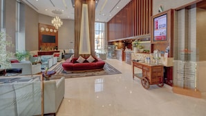 A spacious lobby with a red sofa, a chandelier, a TV, and a digital information board. - Hawthorn Suites by Wyndham Abu Dhabi City Centre (Abu Dhabi)