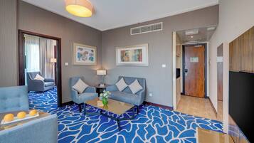 Habitación de hotel con alfombra azul estampada, dos sofás, una mesita de centro y un televisor.