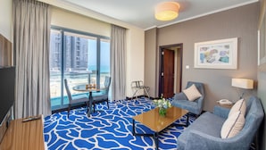 A hotel room with a large window, a blue patterned carpet, a sofa, a coffee table, and a TV. - Hawthorn Suites by Wyndham Abu Dhabi City Centre (Abu Dhabi)