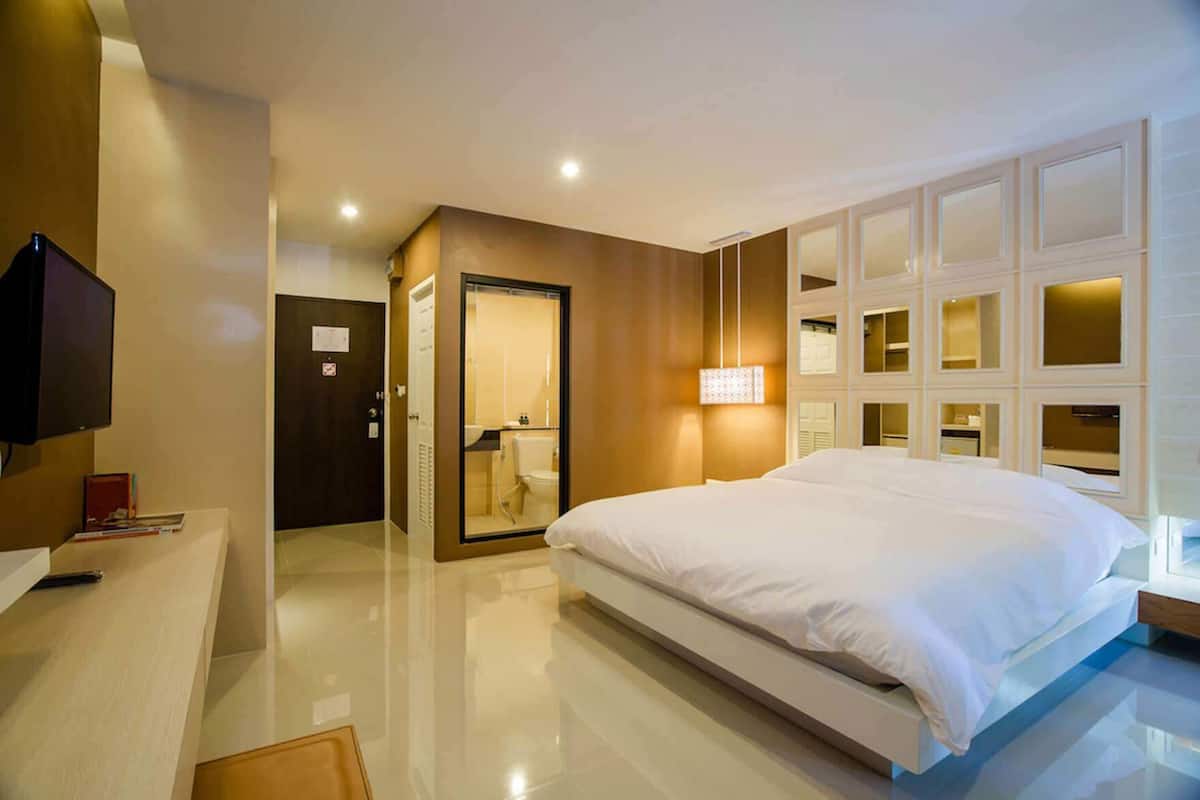 Habitación de hotel moderna con una cama grande, televisión, escritorio y baño visible a través de una puerta abierta.