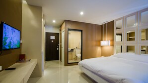 A modern hotel room with a large bed, a television on the left, and a bathroom visible through a glass door. - Naka Residence (Wichit)