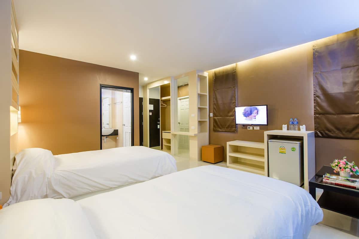 Habitación de hotel con dos camas, televisión, minibar y escritorio con computadora.