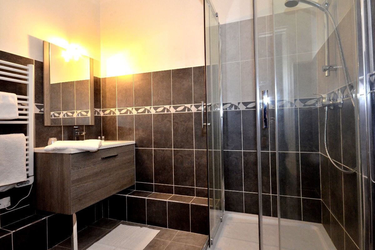 Un baño moderno con ducha de vidrio, tocador de madera y salpicadero de azulejos.