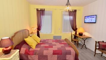 A bedroom with a bed, a desk, a chair, a television, and a lamp.
