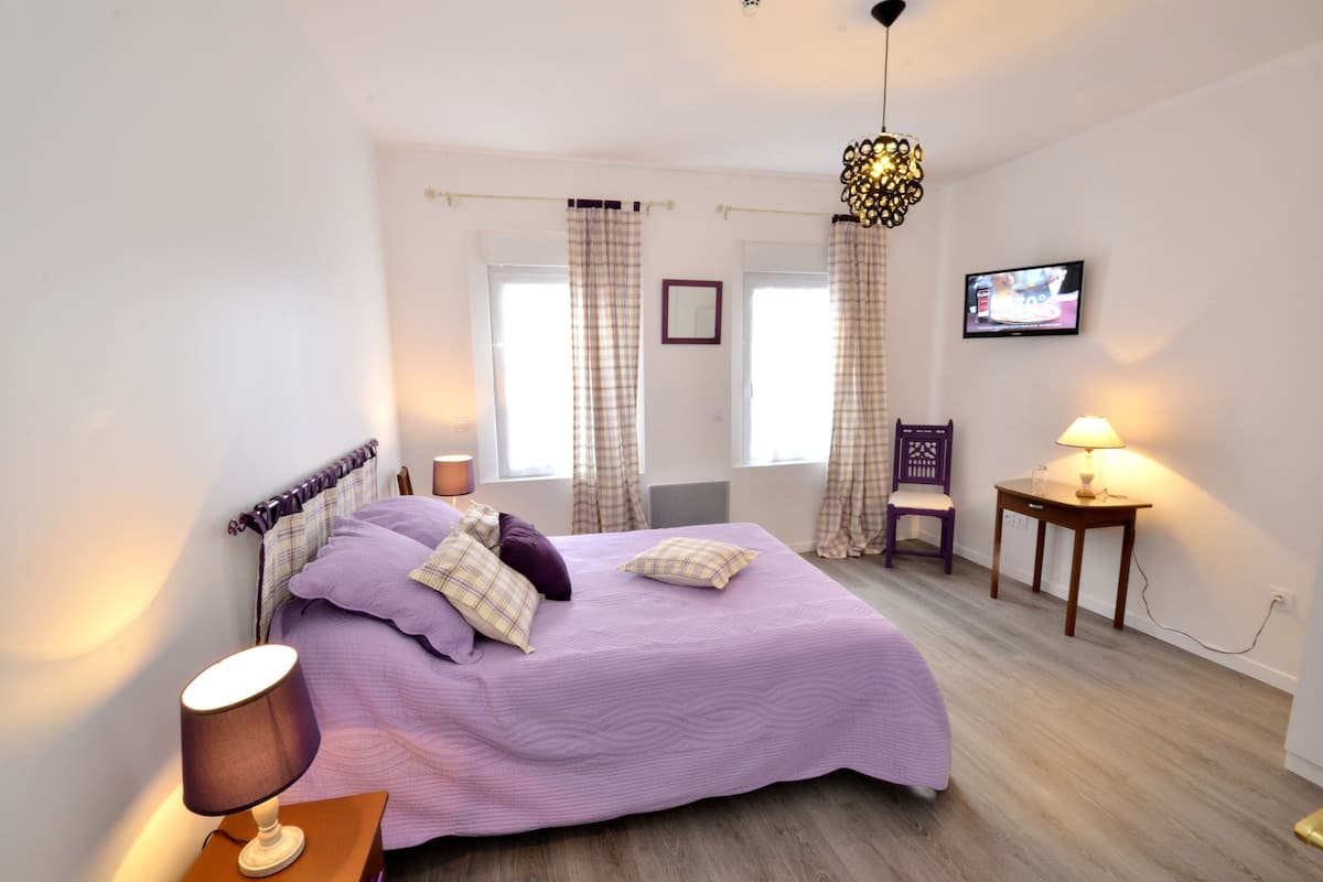 A bedroom with a bed, a chair, a TV, and a lamp.