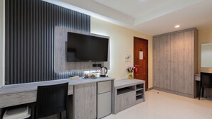A modern kitchen with a built-in TV, wooden cabinets, and a dining area with a chair. - Square One Hotel Patong (Patong)