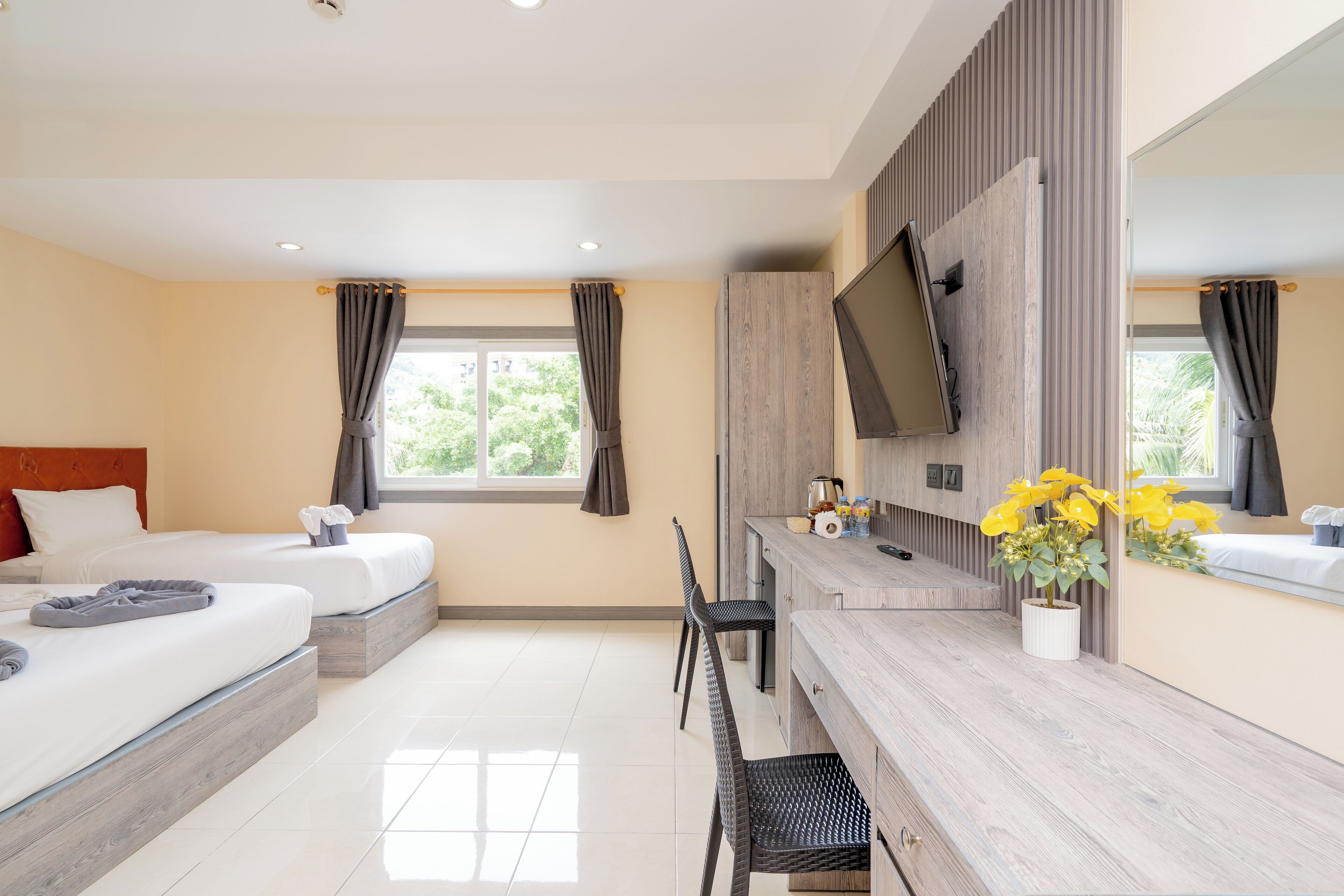 A hotel room with two beds, a desk, a chair, a TV, and a window with curtains.