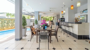 A modern kitchen with a bar area, dining set, and a view of a swimming pool. - Square One Hotel Patong (Patong)