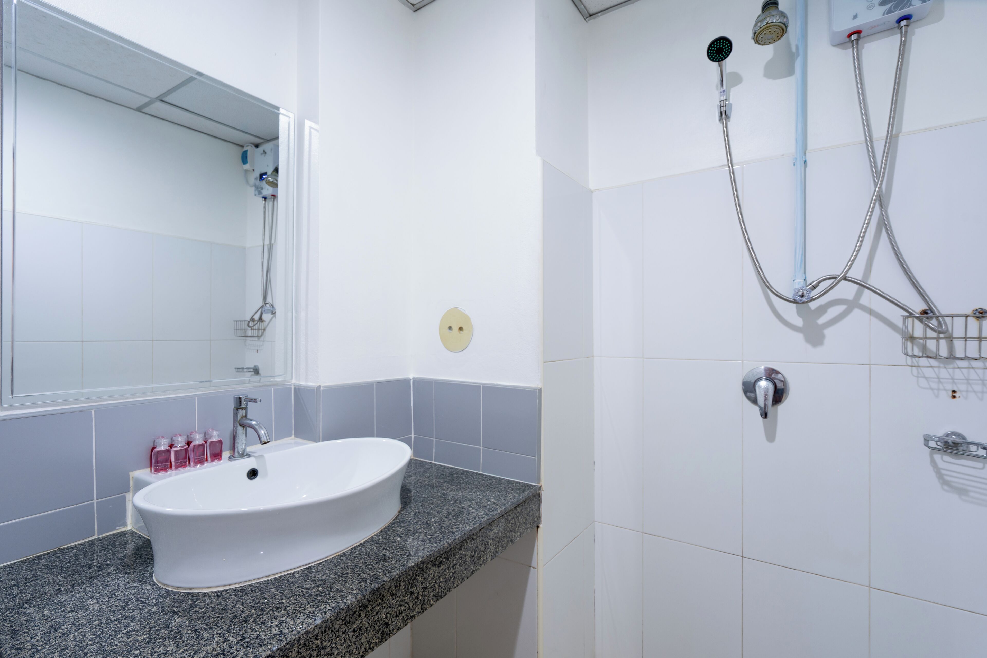 Un baño con un lavamanos blanco, un espejo y una zona de ducha con cabezal de ducha de mano y cabezal de ducha empotrado.