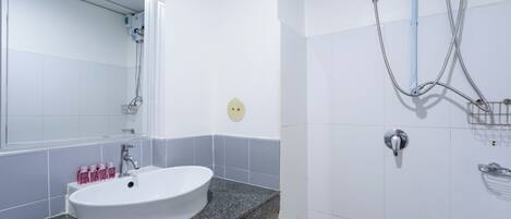 Un baño con un lavamanos blanco, un espejo y una zona de ducha con cabezal de ducha de mano y cabezal de ducha empotrado.