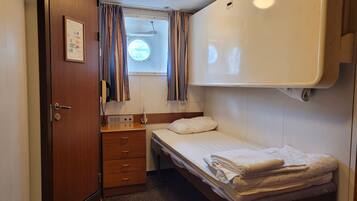 Un dormitorio compacto con una cama individual, una mesita de noche pequeña, una cómoda con cajones, una ventana con cortinas y una lámpara en el techo.