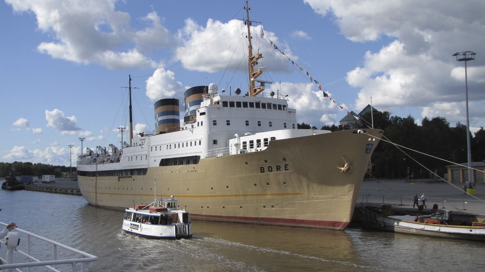 A large ship docked at a port with a smaller boat in front.