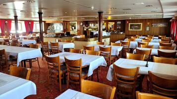 Un restaurante con varias mesas y sillas, una zona de bar y una cocina visible al fondo.
