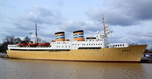 A large, yellow ship with the name "Bore" on its side, docked at a port with other vessels and buildings in the background. - Laivahostel S/S Bore (Turku)