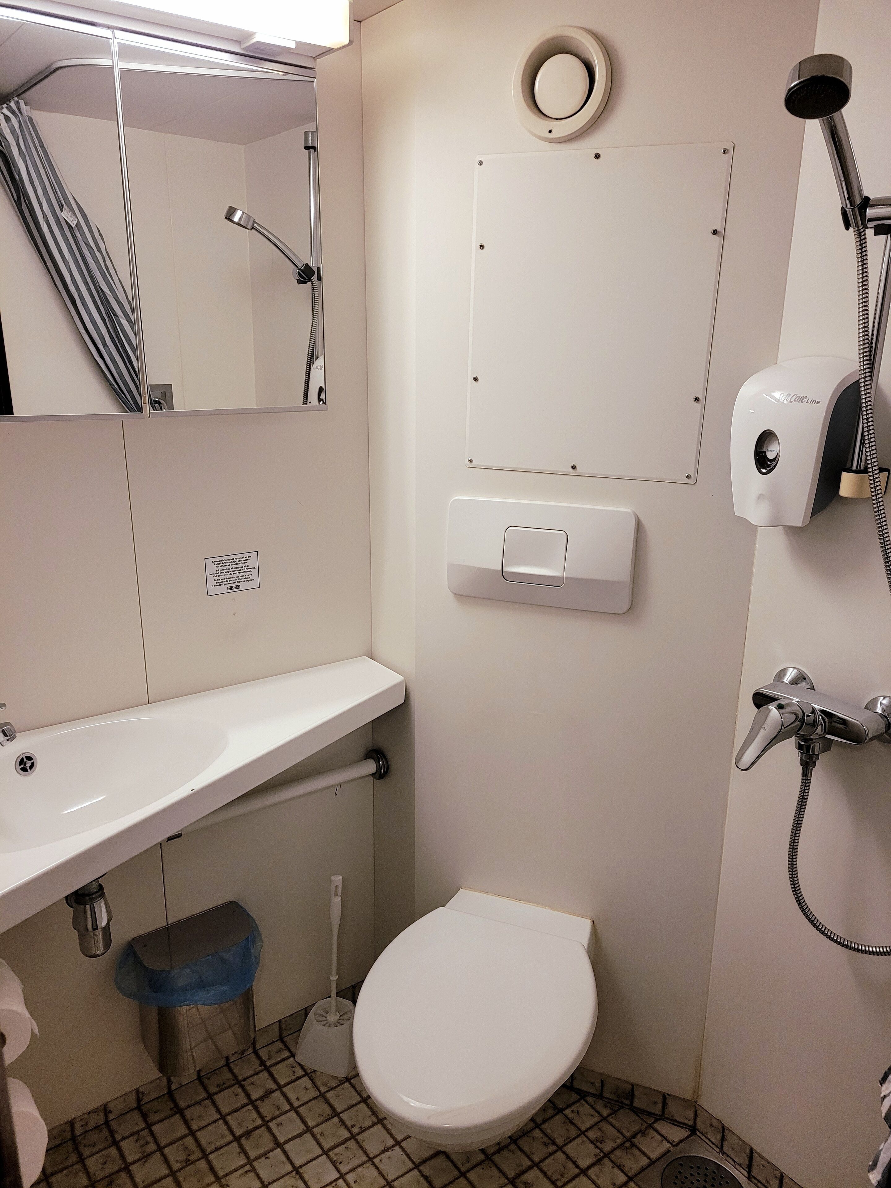 A small bathroom with a white sink, toilet, and shower. There is a mirror above the sink and a towel rack on the wall.