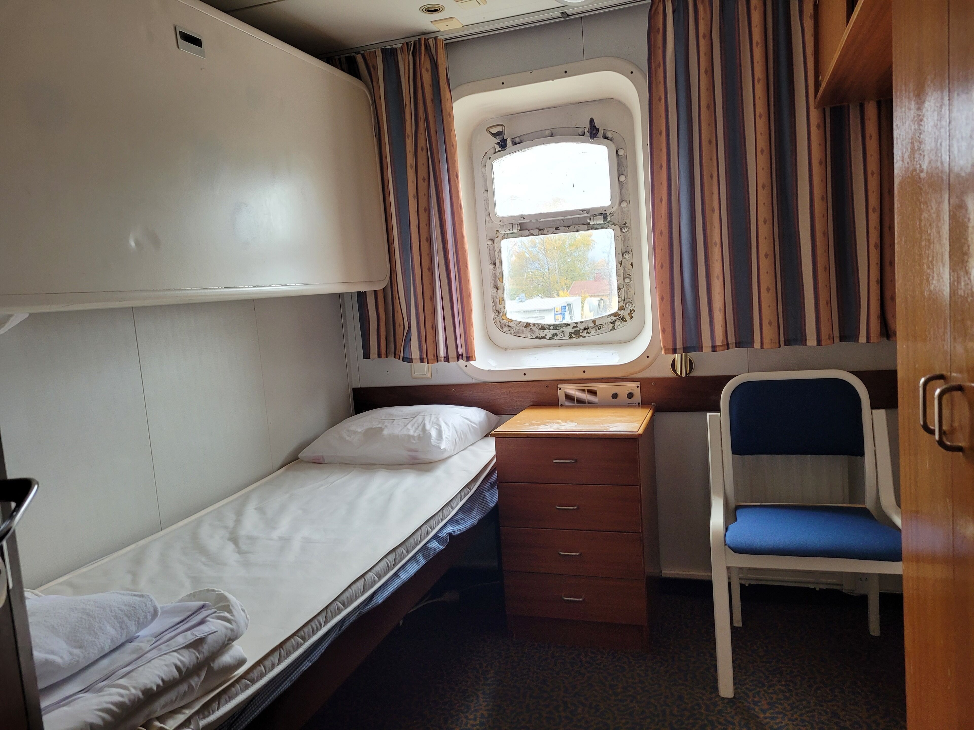 Un compartimento de tren compacto con una cama individual, un escritorio pequeño, una silla y una ventana con cortinas.