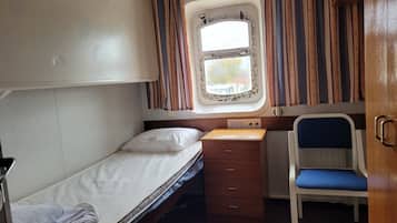 Un compartimento de tren compacto con una cama individual, un escritorio pequeño, una silla y una ventana con cortinas.