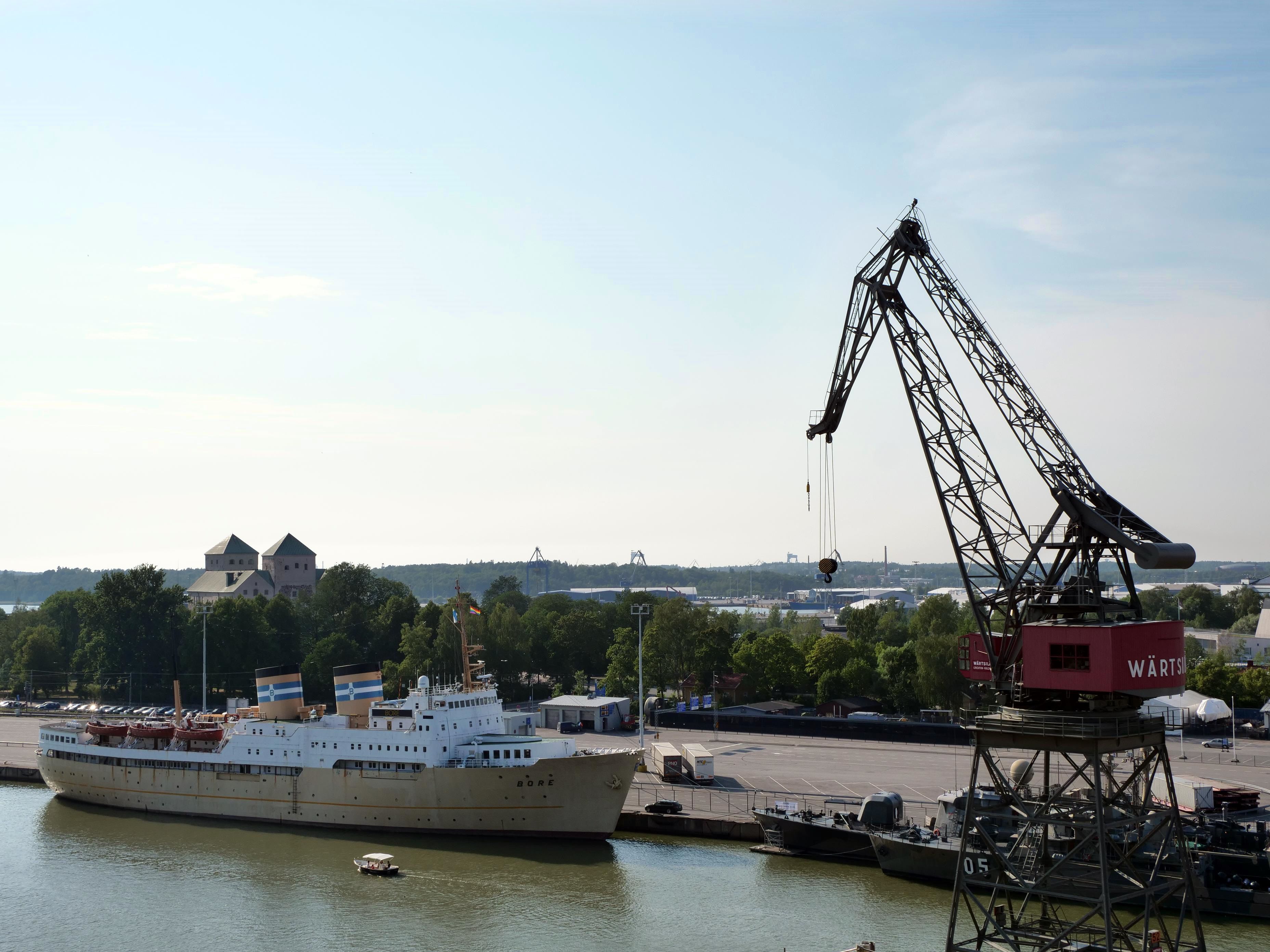 A large cargo ship docked at a port with cranes and industrial buildings in the background.