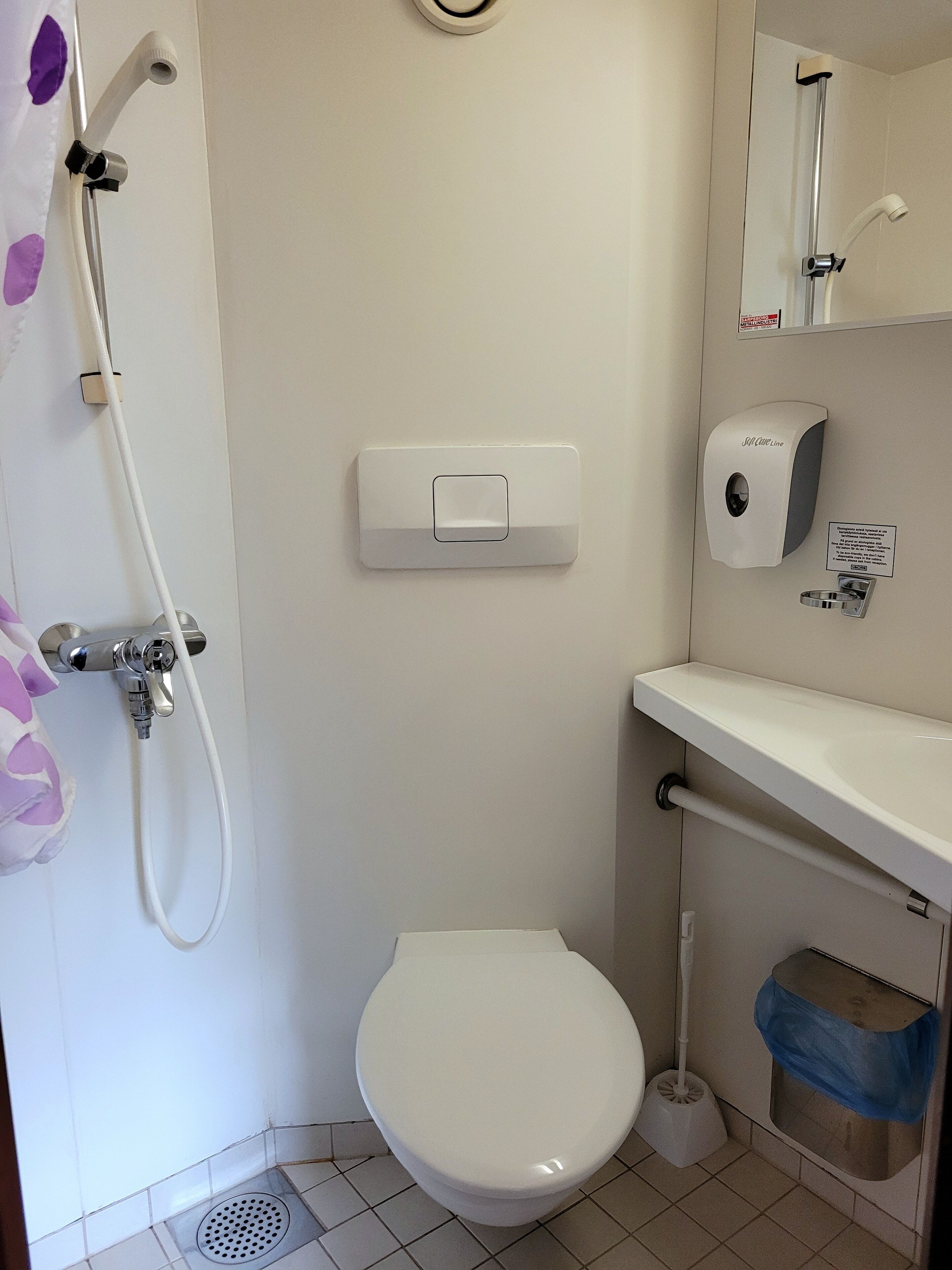 Un baño pequeño y limpio con inodoro, ducha y dispensador de jabón.