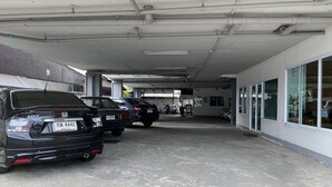 Un área de estacionamiento techada con varios coches y motocicletas, piso de concreto y un edificio con ventanas grandes y una puerta a la derecha.