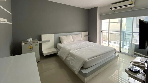 Habitación de hotel moderna con una cama grande, una mesita de noche, un refrigerador pequeño, un televisor de pantalla plana y una ventana con vistas al exterior.
