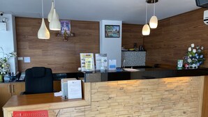 Una recepción con un panel de madera, una silla de oficina negra y una silla roja. Hay luces colgantes, una pequeña estatua de Buda y un cuadro enmarcado en la pared.