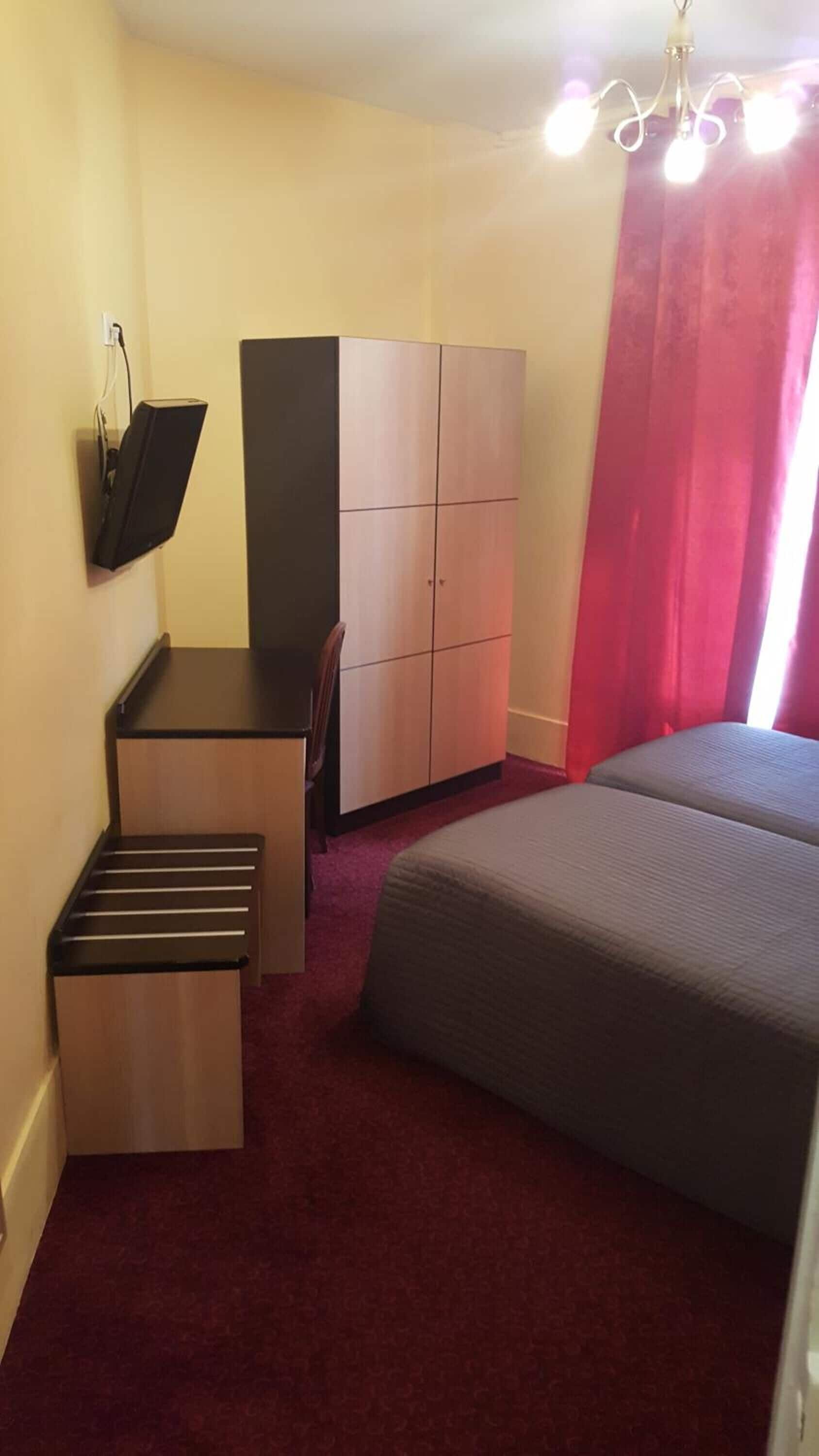 A bedroom with a bed, a desk, a wardrobe, and a TV mounted on the wall.