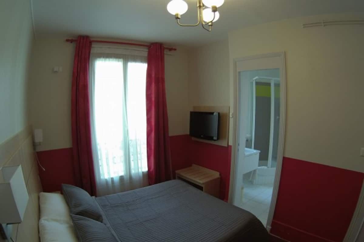 A bedroom with a bed, a television on a stand, and a door leading to a bathroom.
