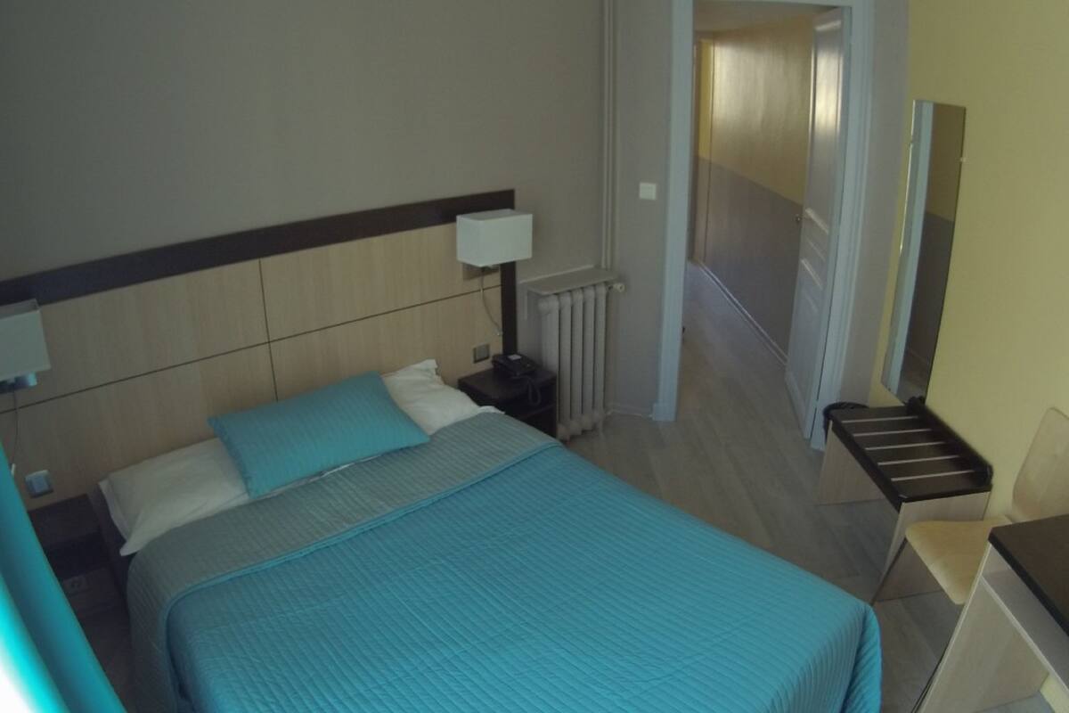 A hotel room with a bed, bedside tables, a lamp, a chair, and a mirror.