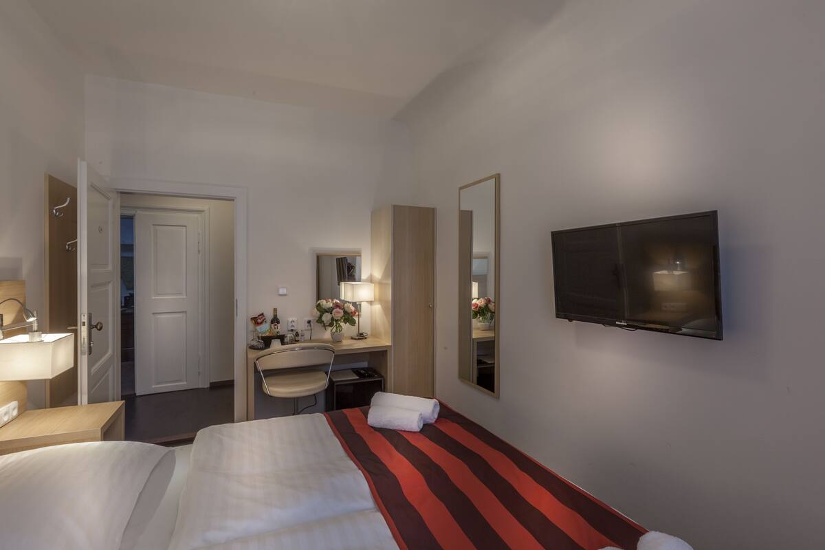 A hotel room with a bed, a desk, a chair, a TV, and a mirror.